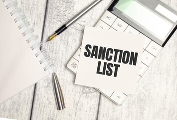 text SANCTION LIST on brown diary with calculator, glasses on wooden background