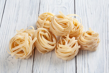 Uncooked tagliatelle pasta on white wooden backgrond