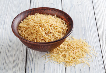 Uncooked vermicelli pasta in ceramic bowl on white wooden background