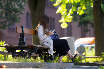 Long haired young woman sitting on wooden park bench with mobile phone at border of Rhine River on...