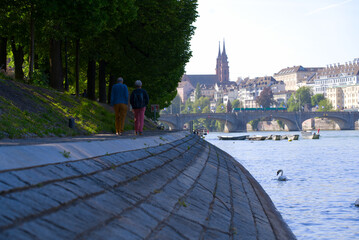 Senior couple walking along of waterfront of Rhine River with skyline of the old town in the background on a sunny spring day. Photo taken May 11th, 2022, Basel, Switzerland.
