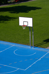 Empty outdoor basketball court with blue floor and basketball basket at park at City of Basel on a sunny spring day. Photo taken May 11th, 2022, Basel, Switzerland.