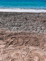 Year 2023 written at the sand beach with sea wave water, heart of stones, holidays in Turkey