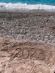 Year 2023 written at the sand beach with sea wave water, heart of stones, holidays in Turkey