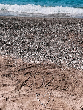 Year 2023 written at the sand beach with sea wave water, heart of stones, holidays in Turkey