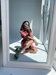 Fit tanned woman in comfy cotton summer long cute dress and green heels, take photo selfie on phone in mirror for social media, stories, vertical.