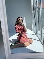 Fit tanned woman in comfy cotton summer long cute dress and green heels, take photo selfie on phone in mirror for social media, stories, vertical.