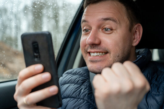 Happy excited millennial man looking at smartphone screen and showing yeah gesture in car