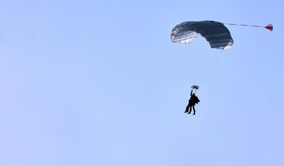 A skydiver with a white parachute canopy against a blue sky and white clouds, close-up.
