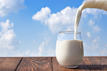 milk pouring from jug into glass on table