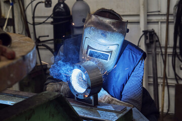 work of a welder, in a chrome welding helmet, blue glow