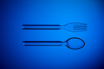 Set of plastic transparent spoon and fork on a blue background.