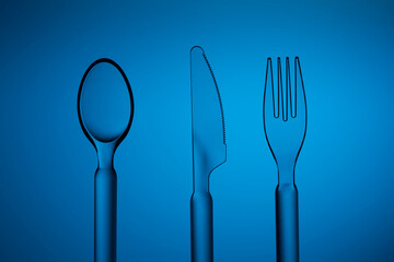 Set of plastic transparent spoon, knife and fork on a blue background.
