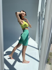 Obraz premium Fit tanned woman in sportswear, fitting blue leggings, perfect body, abs motivation, take photo selfie on phone in mirror for social media, stories, vertical.