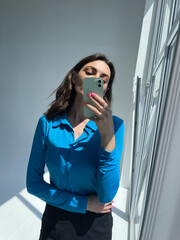 Fit tanned woman in classic short black skirt and blue blouse, take photo selfie on phone in mirror...