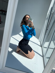 Fit tanned woman in classic short black skirt and blue blouse, take photo selfie on phone in mirror for social media, stories, vertical.