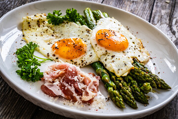 Sunny side up eggs with green asparagus  fried bacon on black plate on wooden table
