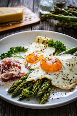 Sunny side up eggs with green asparagus  fried bacon on black plate on wooden table
