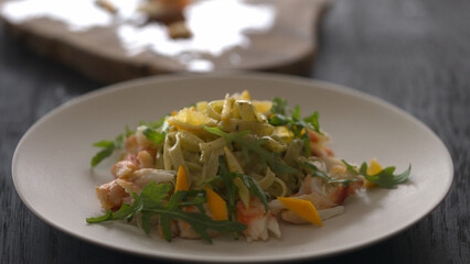 serving fettuccine with crab meat, lemon and arugula on white plate closeup