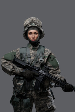 Shot of special forces woman dressed in protective uniform holding rifle isolated on gray background.