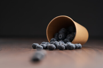 Ripe blueberries spilling from paper cup on wood table