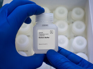 Close-up, two hands in blue gloves hold a white chemical reagent bottle, assay buffer, reagent kit...