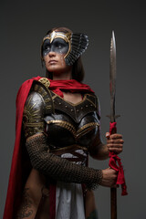 Studio shot of ancient woman soldier dressed in steel armor with cape holding spear.