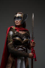 Obraz premium Studio shot of ancient woman soldier dressed in steel armor with cape holding spear.