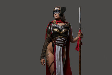 Studio shot of wild female warrior from past with painted face holding spear isolated on grey...