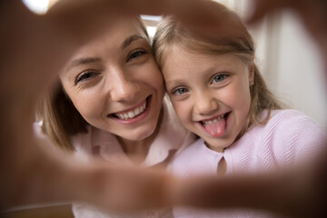 Young cheerful mother and funny little daughter joined their fingers showing hearts symbol on camera, close up happy faces webcam view. Unconditional love, family ties, happy motherhood, fun concept - obrazy, fototapety, plakaty