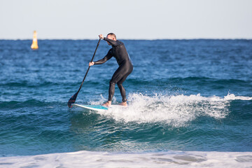 caucasian man stand up paddle ocean water wave surf blue black wetsuit active fit  SUP