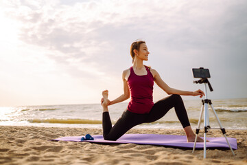 Young sporty  woman yoga coach records video online training yoga on the beach. Sport, Active life.