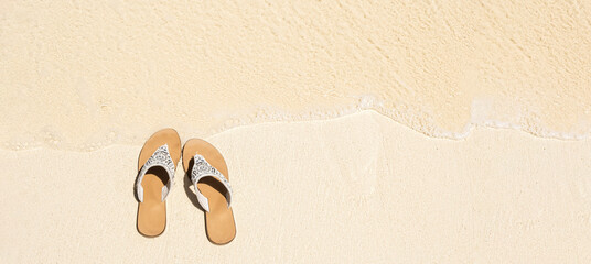 Fototapeta na wymiar Pare of white sandals on wet sand by sea side, top view with copy space, summer concept