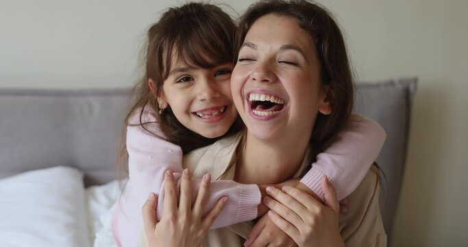 Close up portrait happy mother and little daughter smile look at camera, 6s cute girl piggyback her loving mom posing for cam at home. Life value, unconditional love between child and parent concept