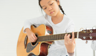 beautiful young children show playing guitar, look at finger. asian children study and learn musical and singing in education classroom at small school