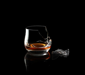 Broken whiskey glass isolated on black background.