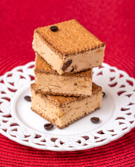 Coffee ice cream with biscuits and ricotta, on a white, round plate and a red background 
