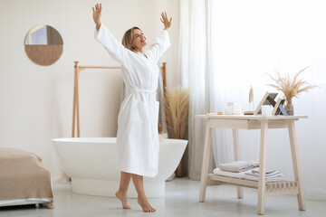 Joyful middle aged lady dancing by white bathroom at home