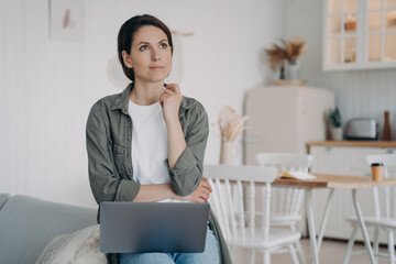 Freelancer is planning future and dreaming. Spahish woman is sitting at computer at cosy kitchen.