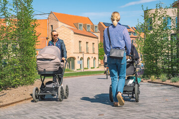 Beautiful young blonde hair girls with stroller walking on a new bike path or road between modern...