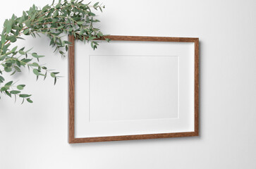 Landscape frame mockup on white wall with fresh eucalyptus. Blank mockup copy space for art, painting or photo.
