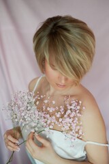 Naklejka premium Portrait of a girl on a pink background with flowers. Tenderness and feminine. The sphere of beauty and women's health. Short haircut, blonde hair