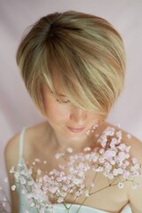 Portrait of a girl on a pink background with flowers. Tenderness and feminine. The sphere of beauty and women's health. Short haircut, blonde hair