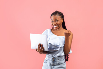 Cheerful black woman with laptop making YES gesture, getting good news online, achieving success,...
