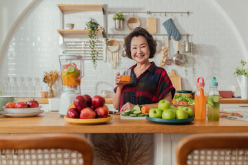 Mature smiling woman cook salad, fruits and vegetables. Attractive mature woman with fresh green fruit salad at home. Senior woman apron standing in the kitchen counter relaxing in house weekend time