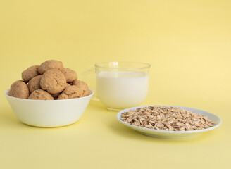 Oatmeal, oatmeal cookies on a white plate, milk in transparent glass on a yellow background, side view, the concept of healthy eating and making cereal or cookies. High-quality photo
