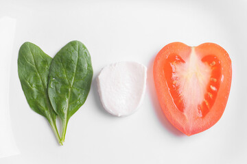 caprese salad from tomatoes, a slice of mozzarella cheese and spinach leaves lie on a white background in the form of an italy flag