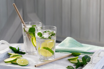 Summer refreshing mojito cocktails with lime and mint on a white wooden tray