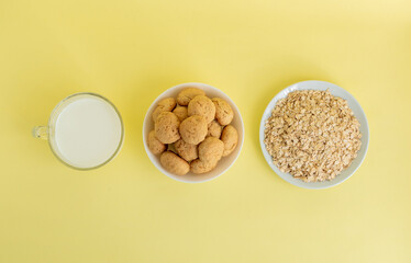 Flatlay oatmeal, oatmeal cookies on a white plate, milk in transparent glass on a yellow background, top view, the concept of healthy eating and making cereal or cookies. High-quality photo