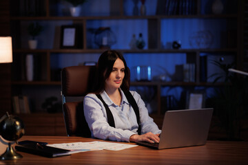 Young woman working with laptop in office. Office worker analyzing graphs and charts, overworks while sitting in the office until late. Cinematic lighting.Business concept